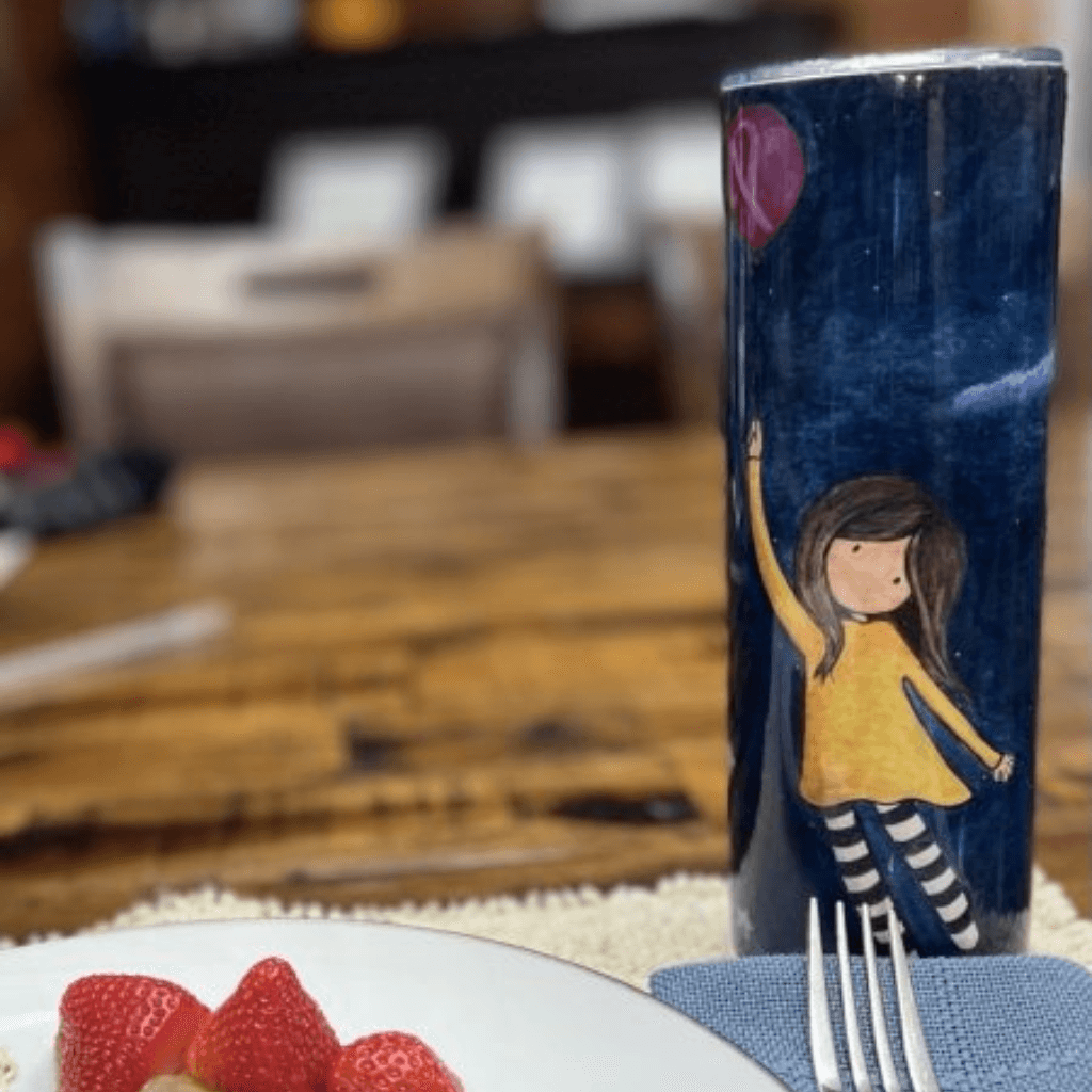 Trust the Journey breast cancer tumbler featuring original watercolor artwork by Kim Chabre, displayed on a breakfast table with strawberries.
