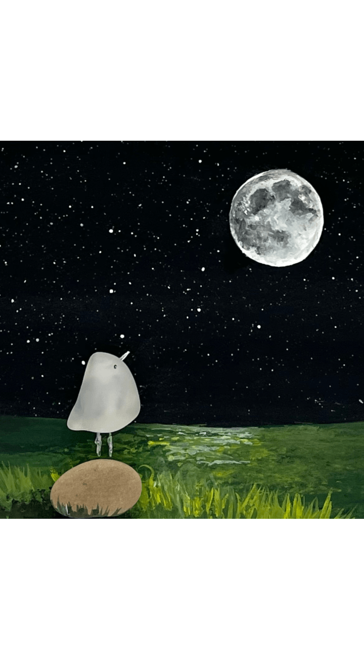 A stylized bird made from river glass standing on a rock, looking toward a full moon and stars in a dark night sky above grass.