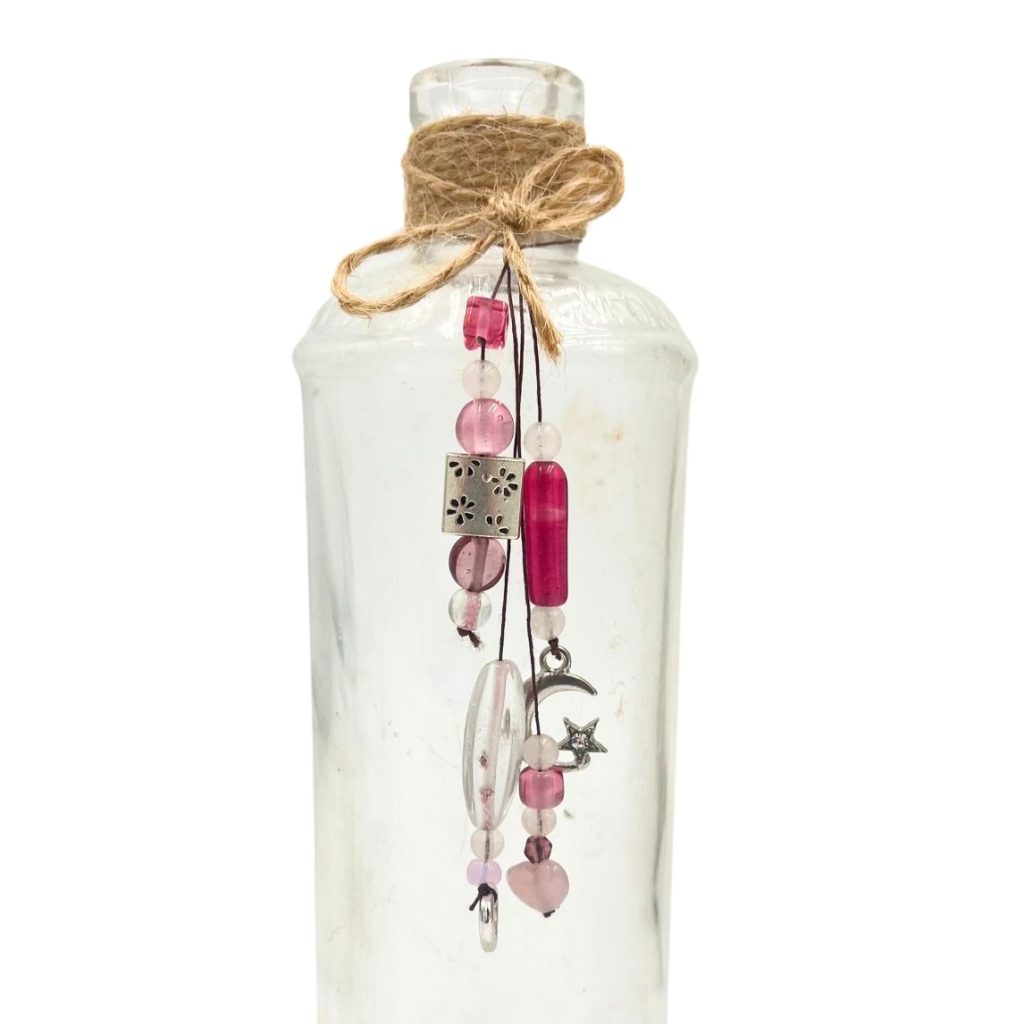 Upcycled LF glass bottle found in the Aroostook River, decorated with pink beads, charms, and twine