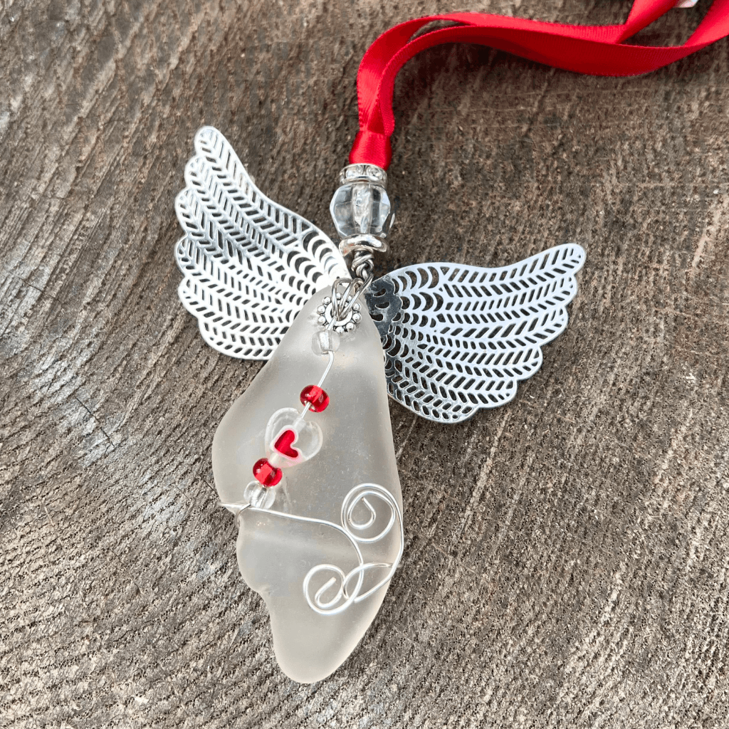 Beach glass angel ornament with silver wings and red heart beads displayed on rustic wood