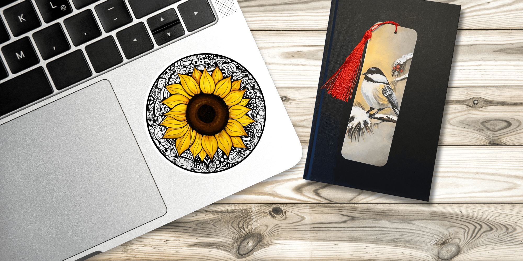 Riverbed Art sunflower sticker on laptop and Winter Chickadee bookmark with tassel on book.