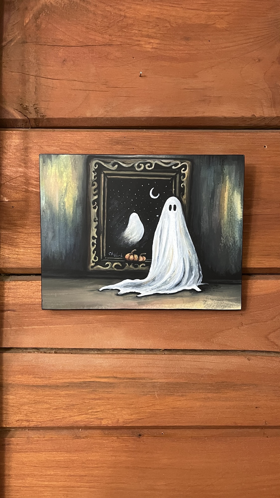 Mounted print of a ghost beside her painting with crescent moon and pumpkins, sold artwork.
