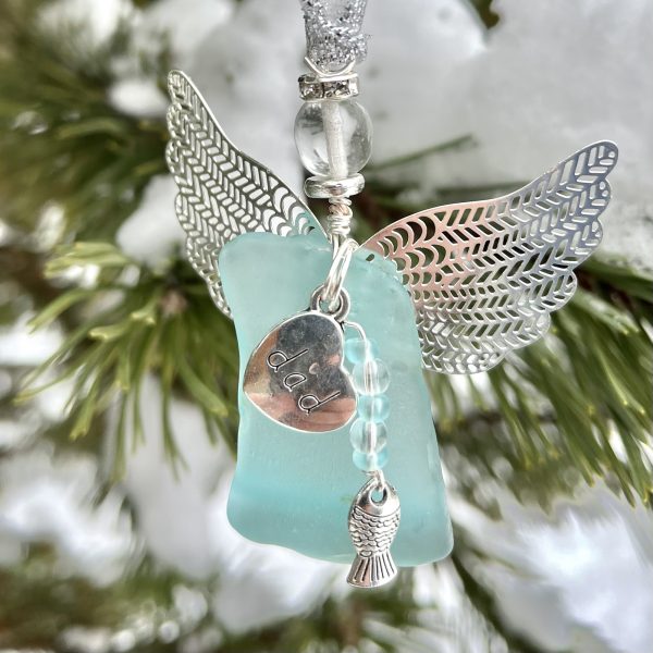 Close-up of Dad’s River Catch beach glass angel with silver wings, “dad” charm, and fish charm outdoors.