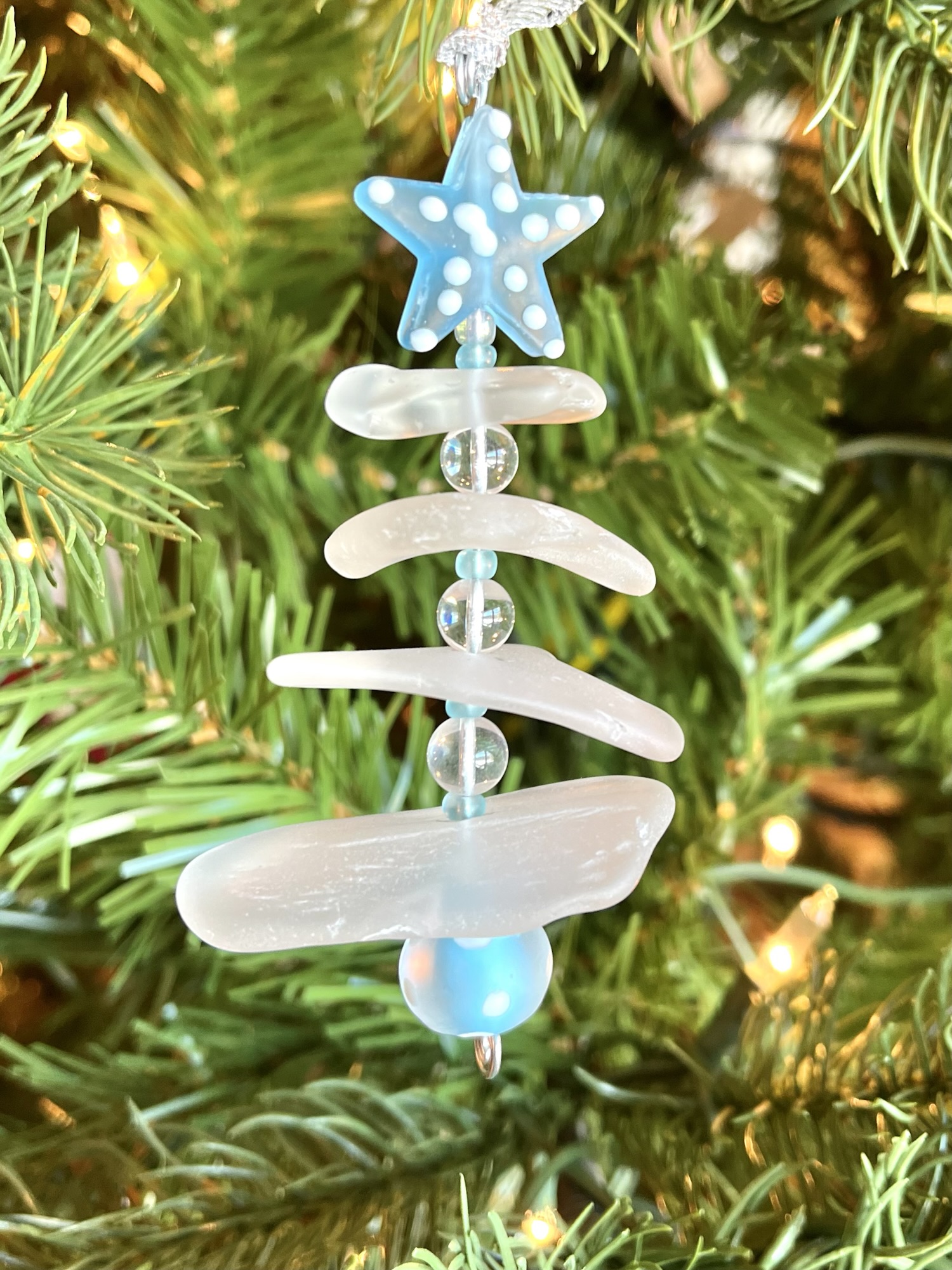 2025 Aroostook River Snow Tree No. 3 hanging on a Christmas tree with warm lights.