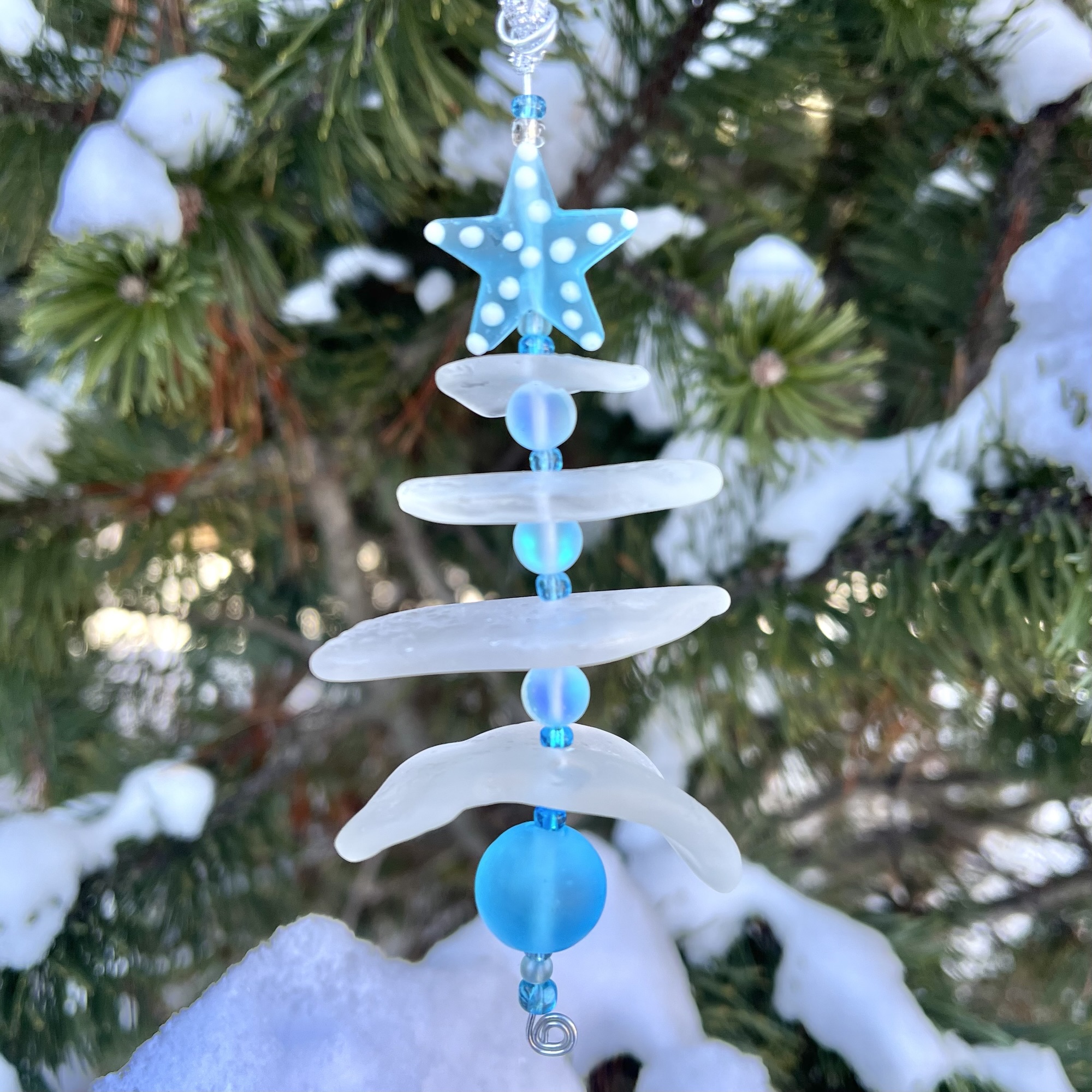 2025 Aroostook River Snow Tree No. 4 hanging outdoors among snowy pine branches.
