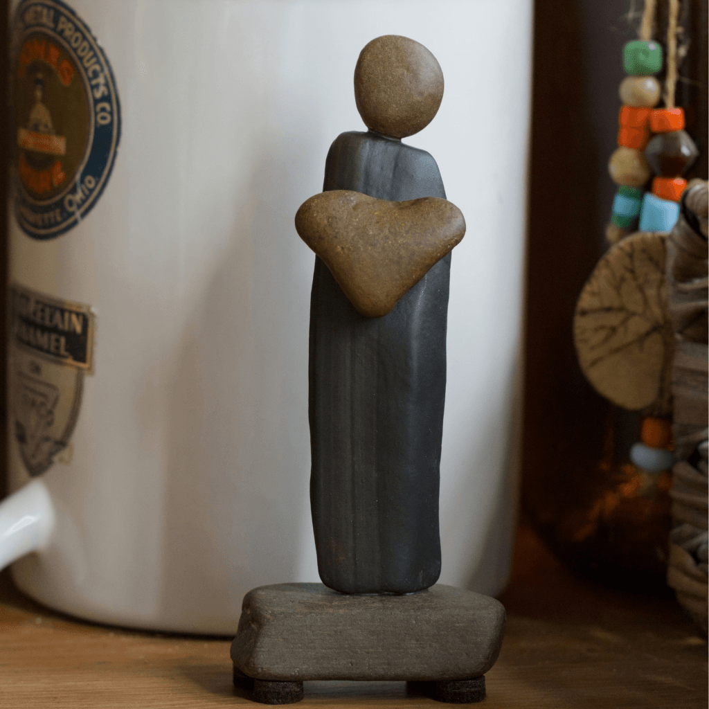 I Give You My Heart stone sculpture displayed on a wooden shelf beside a white crock and colorful beads.