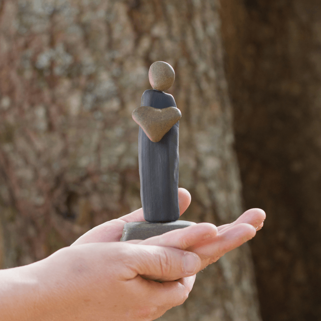 I Give You My Heart river stone sculpture resting in an open hand outdoors to show its scale.