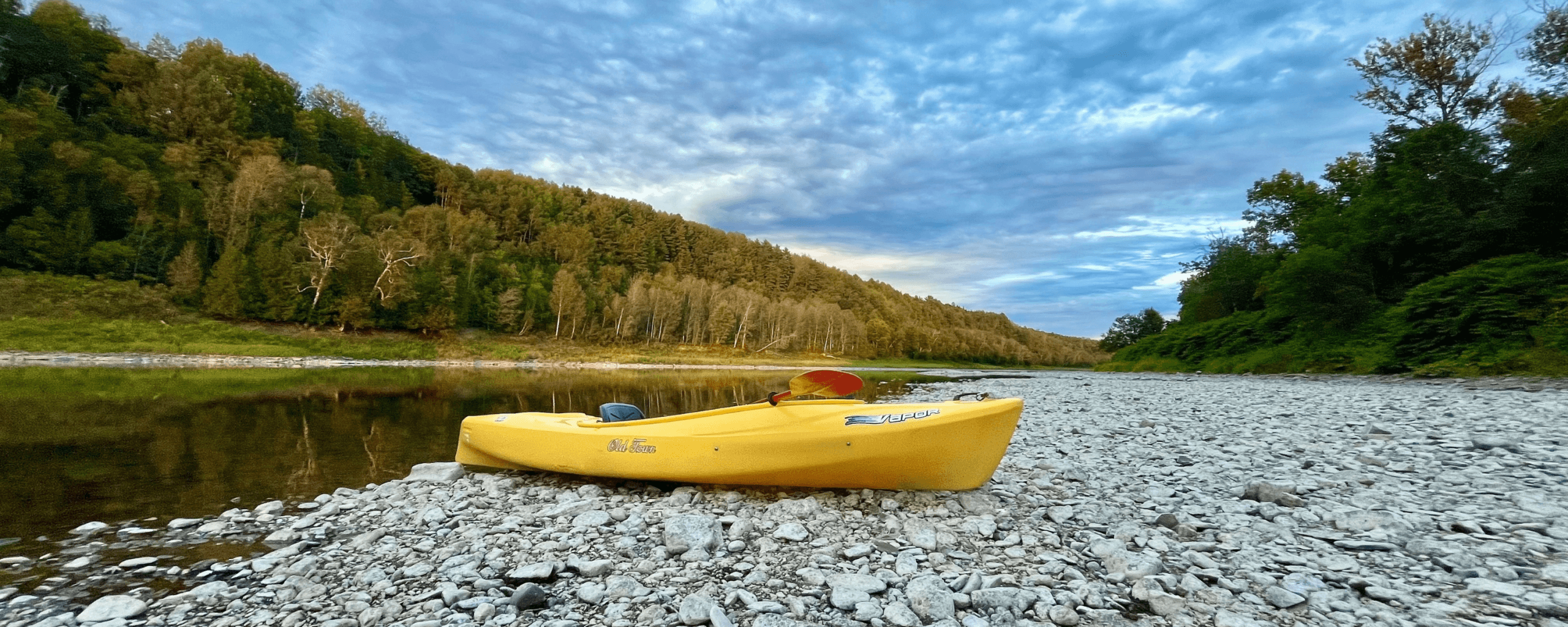 My yellow kayak resting on the exposed rocky Aroostook River bed in Caribou, Maine, during low water.