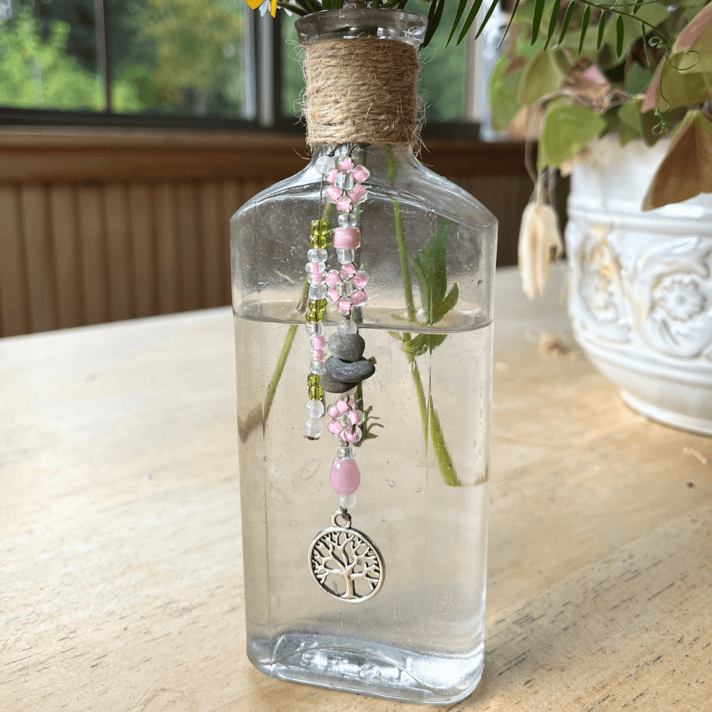 Upcycled vintage BEST bottle from the Aroostook River with stitched seed bead daisies, drilled river stones, pink and green glass beads, and a Tree of Life charm