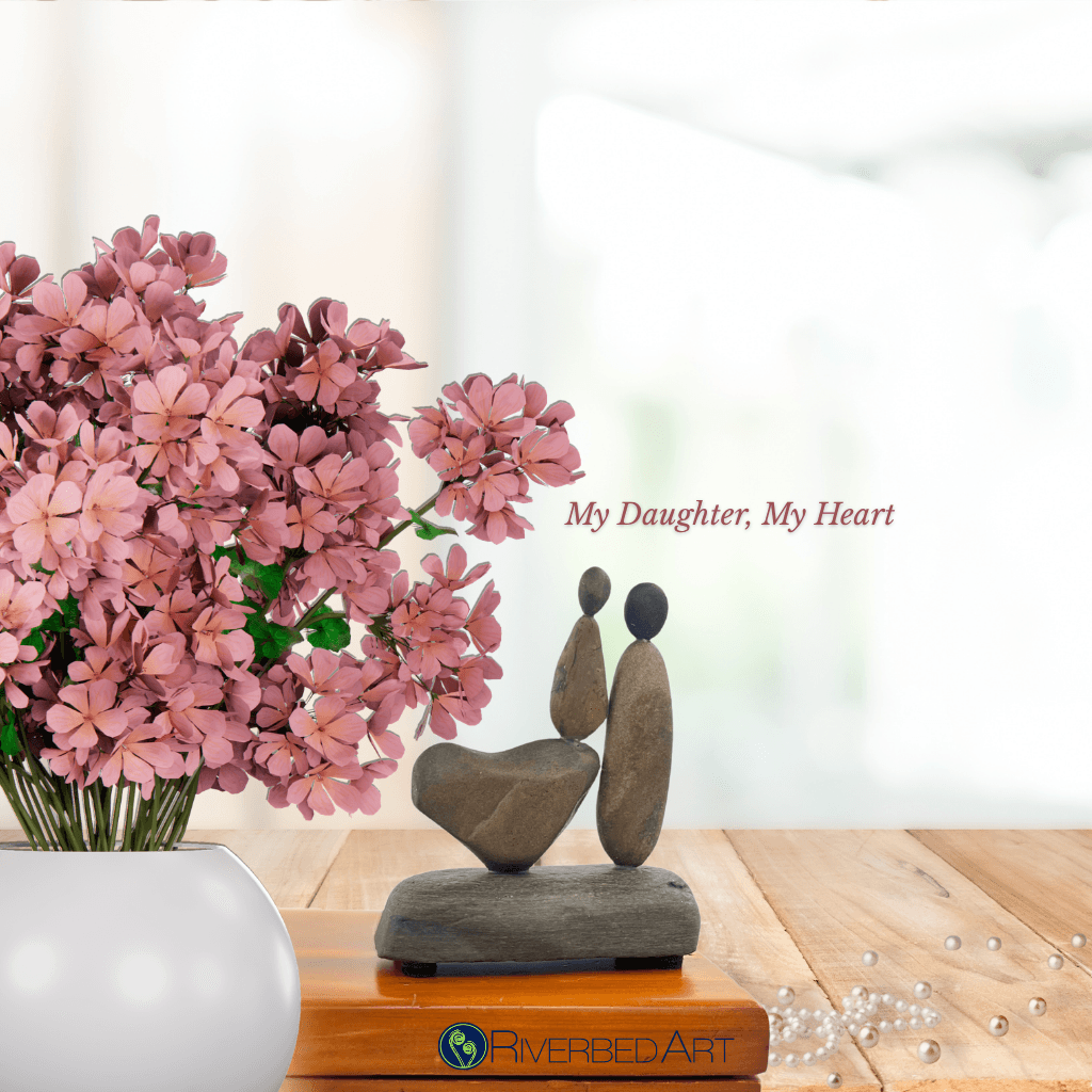 My Daughter, My Heart stone sculpture beside pink flowers, with the artwork title above and Riverbed Art logo below.