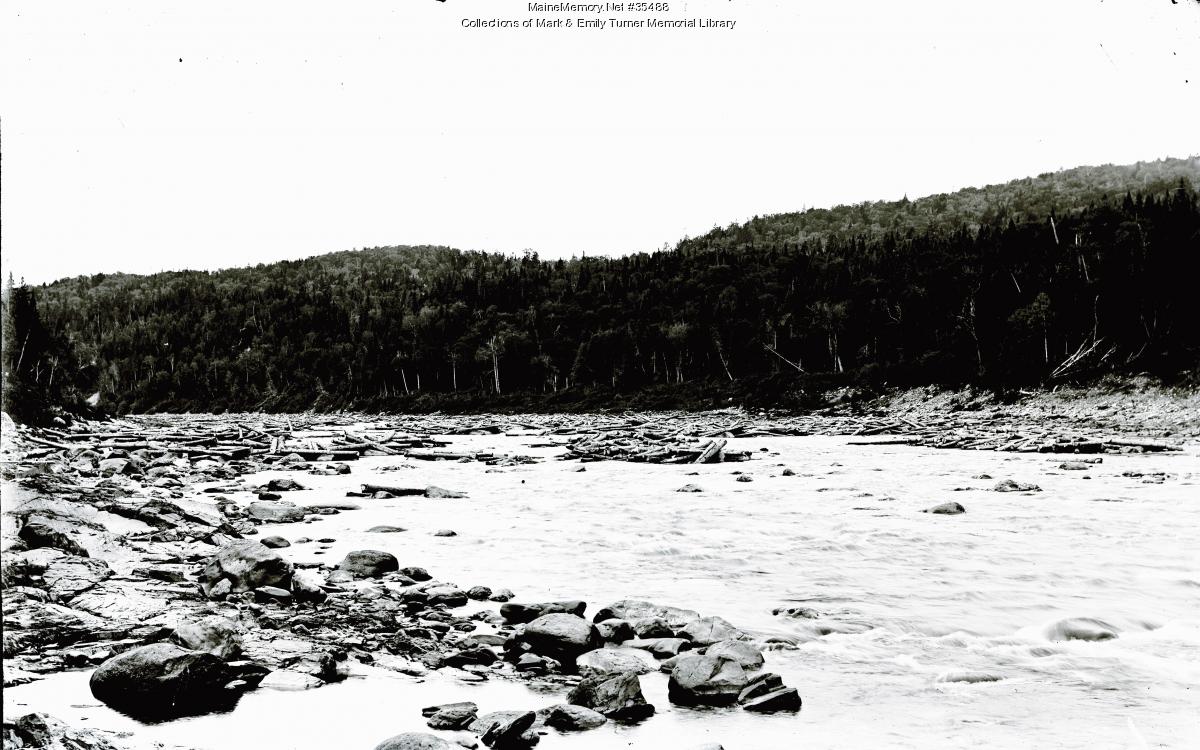 Logs stranded on rocks along the Aroostook River during a low water log drive in Aroostook County, Maine, circa 1900