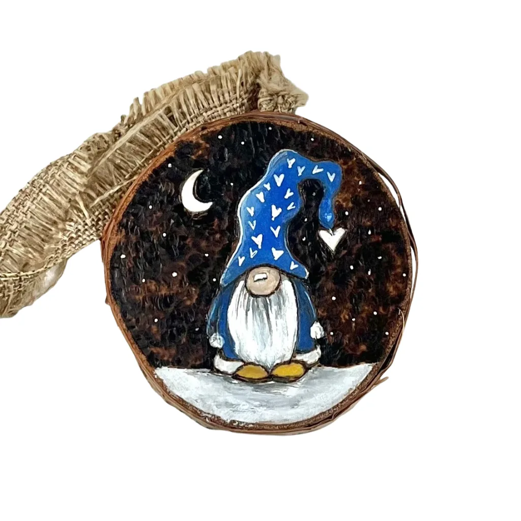 Birch slice ornament with a blue-hatted gnome, white hearts, crescent moon, and hanging ribbon on a white background.