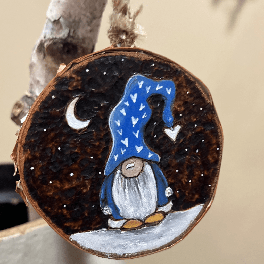 Birch slice ornament with a blue-hatted gnome, white hearts, a crescent moon, and a dark woodburned background