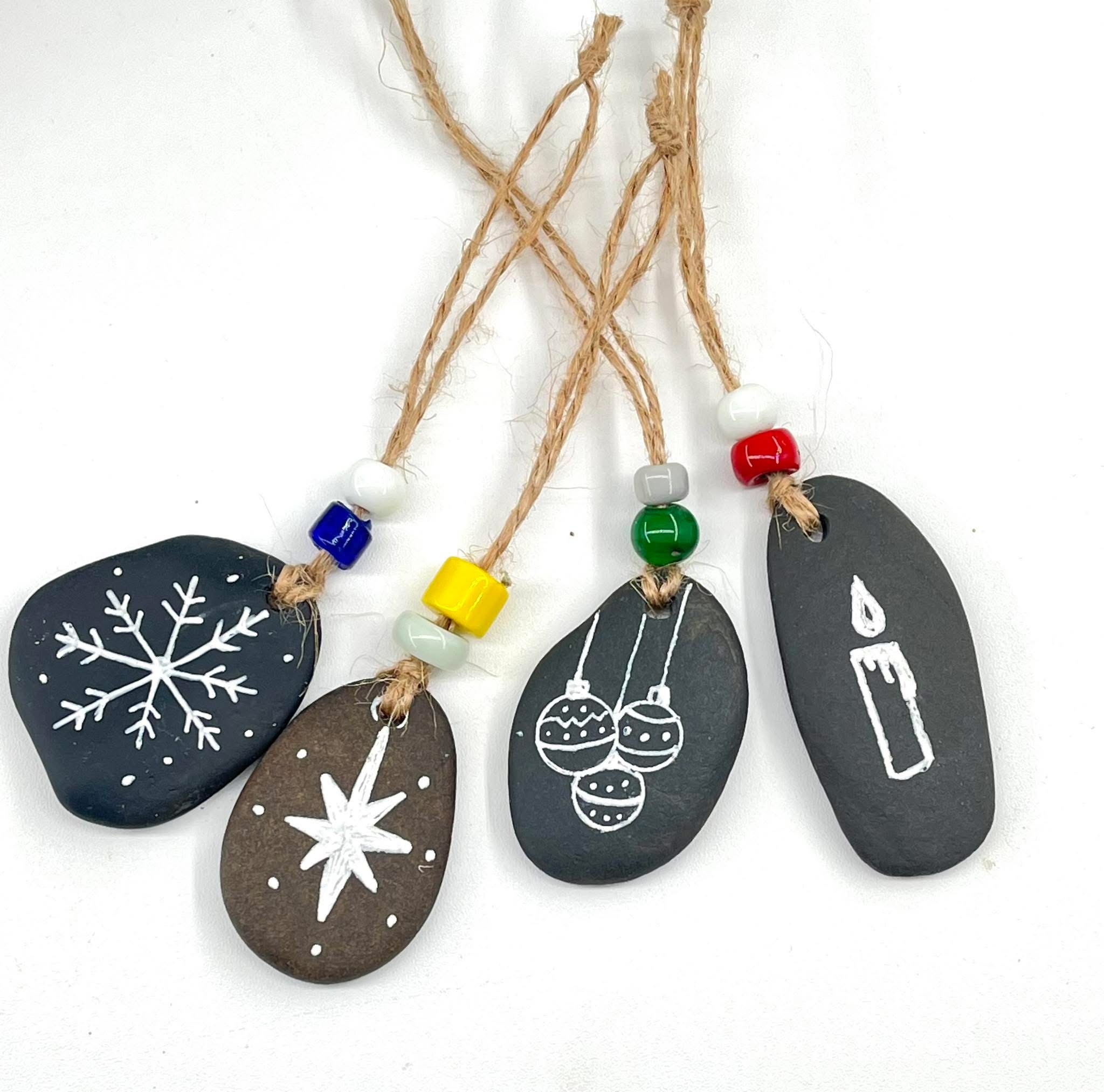 Four drilled river stone Christmas ornaments with white designs, twine, and colored beads