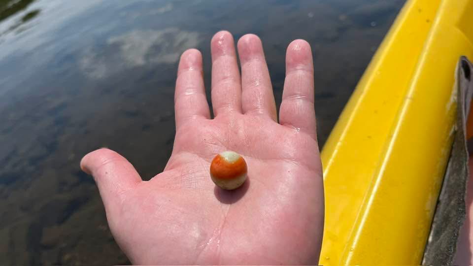 Orange and cream marble in an open hand beside a yellow kayak on the river