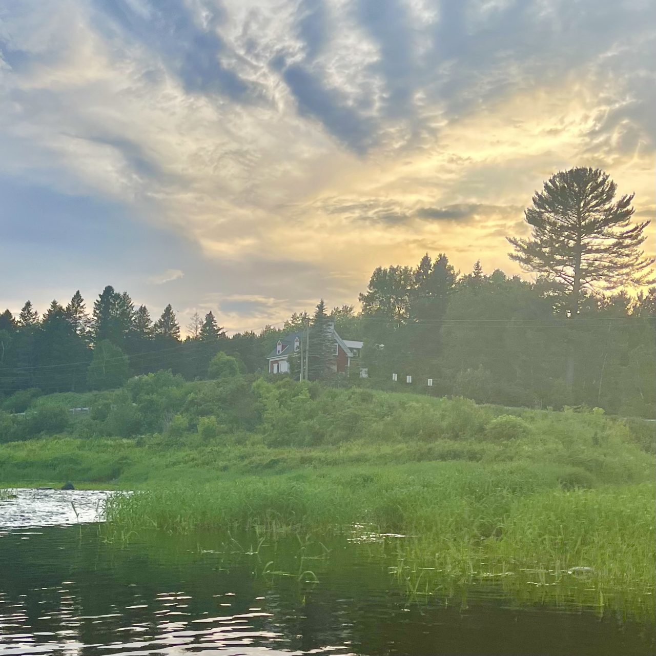 Old Collins house near Otter Brook, seen from the Aroostook River in Caribou, Maine, beneath an evening sky.